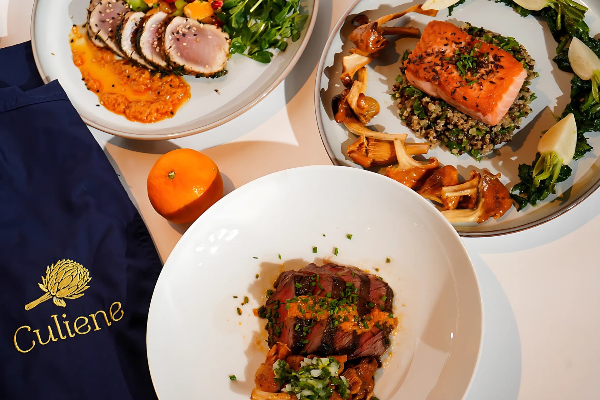 A Culiene apron beside plates of tuna and salmon on a white table