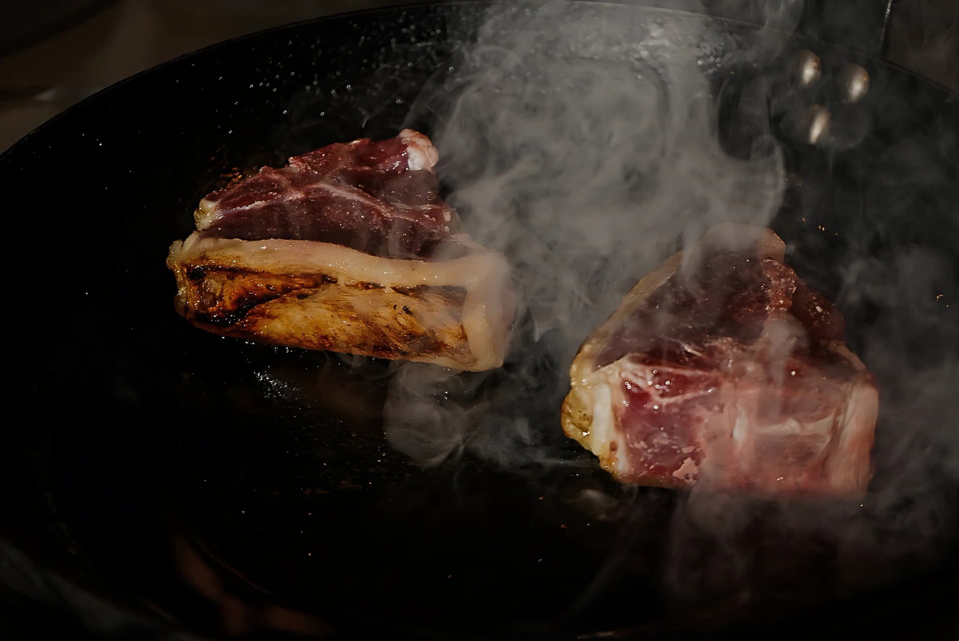 Lamb chops searing in a cast iron pan with smoke rising