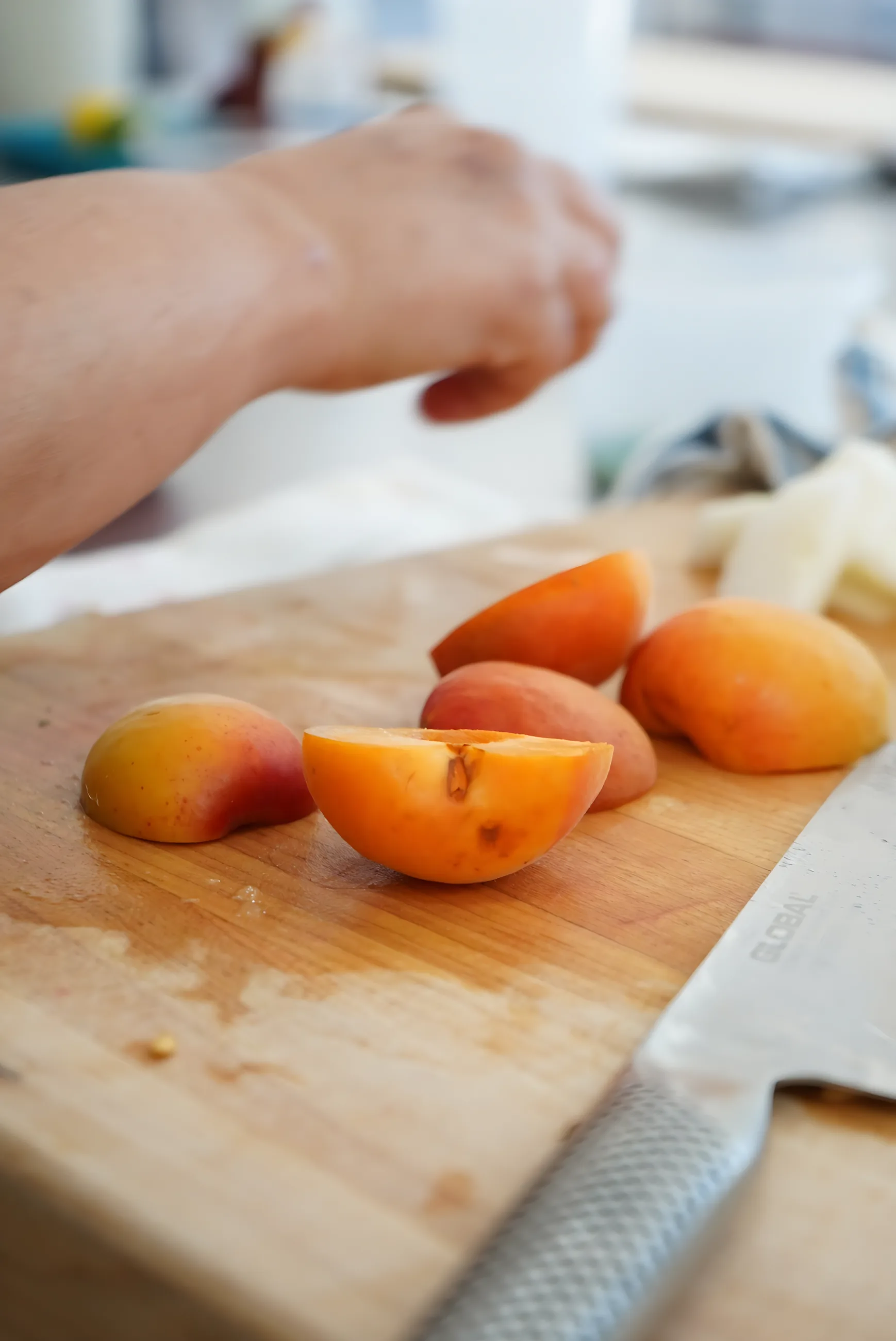 Halving fresh apricots on a wooden cutting board