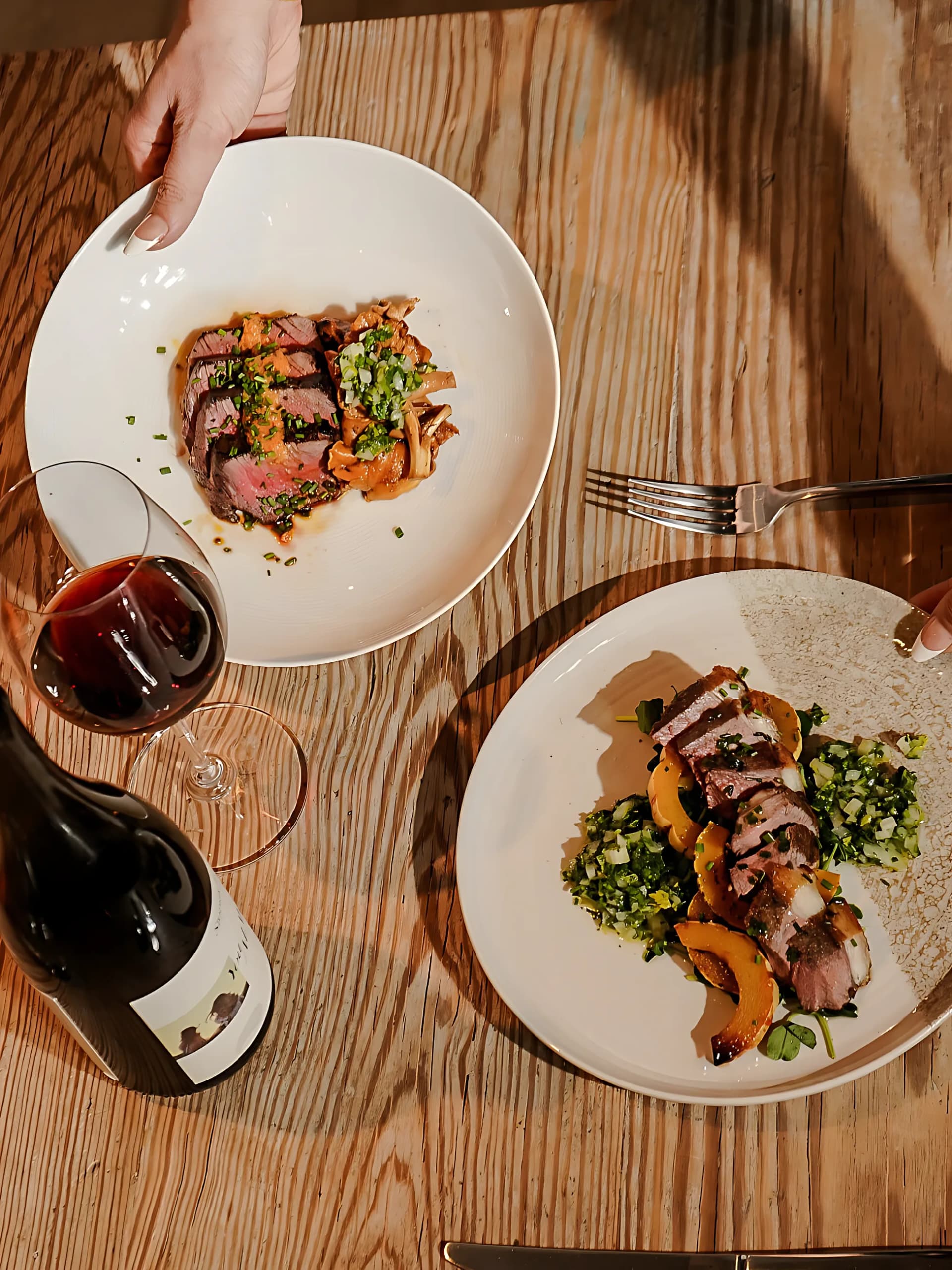 Plates of duck and salmon on a wooden table with a glass of red wine